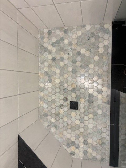 A shower stall with a hexagonal tile floor in a bathroom.