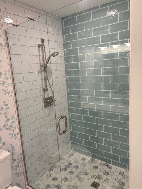 A bathroom with blue tiles and a walk in shower with a glass door.