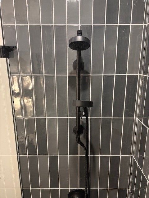 A black shower head is sitting on a tiled wall in a bathroom.