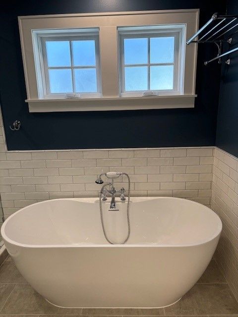 A bathtub in a bathroom with a window above it