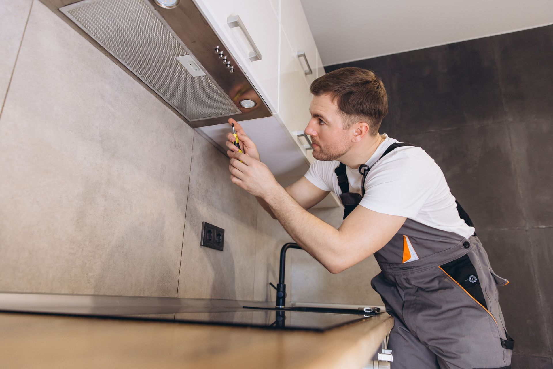 A man is fixing a kitchen hood with a screwdriver.
