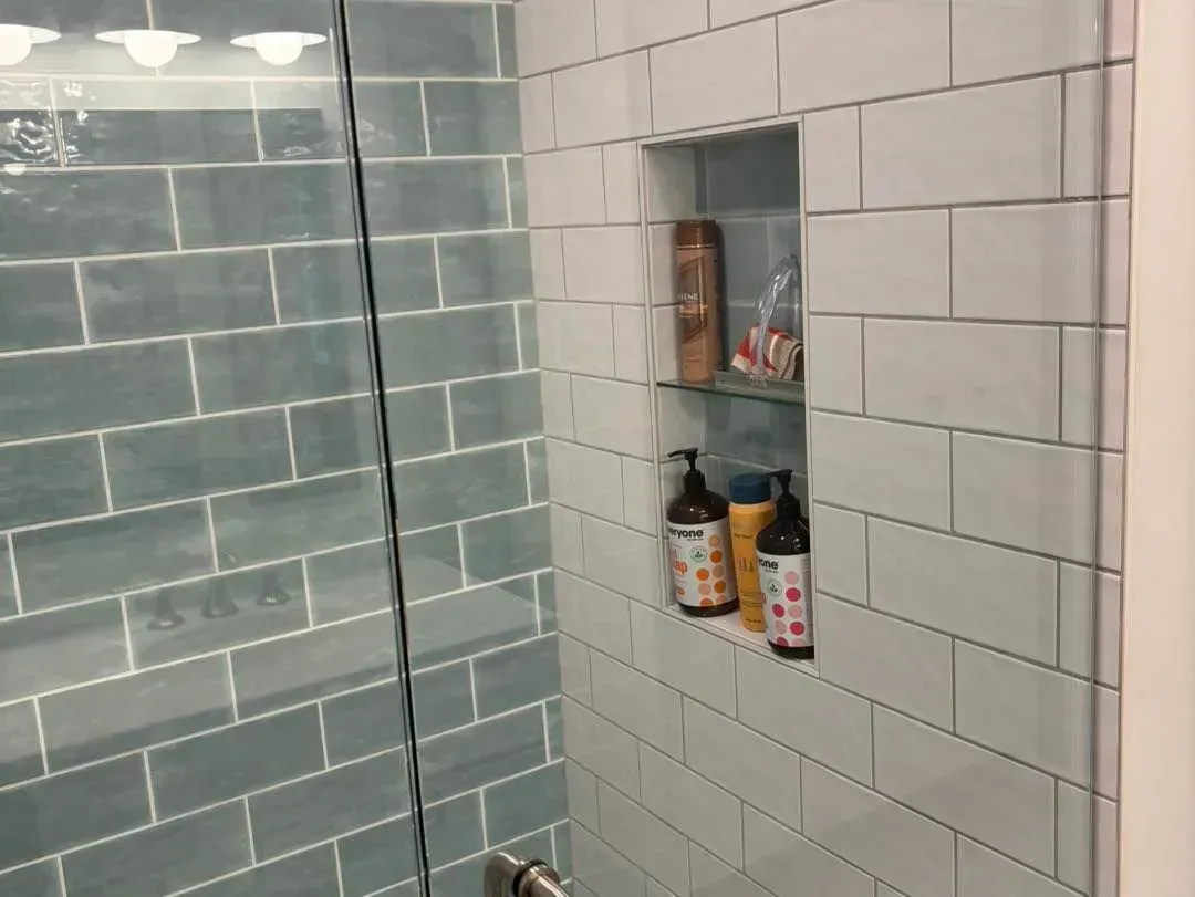 A bathroom with white tiles and a glass shower door.