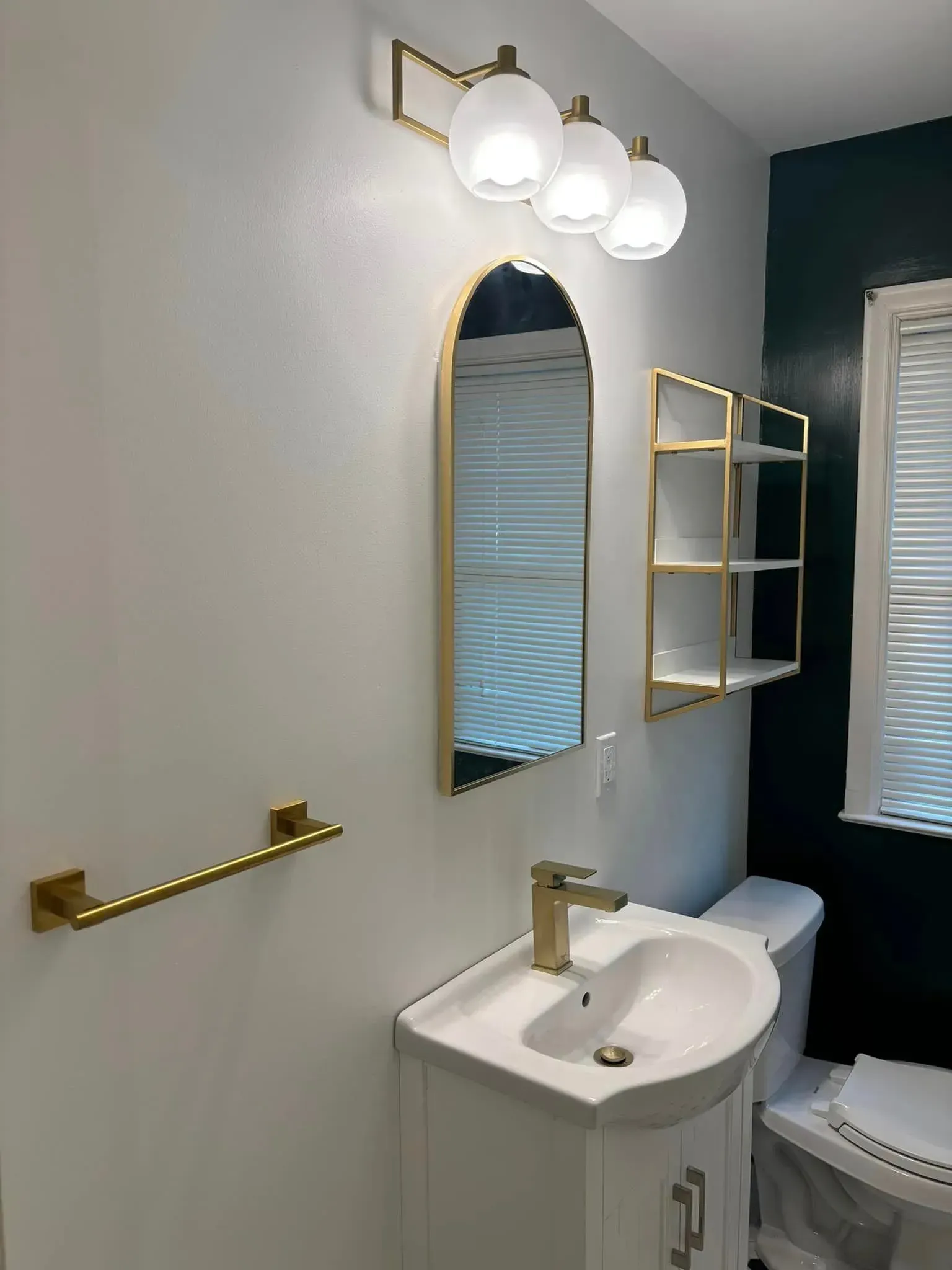 A bathroom with a sink , toilet , mirror and shelves.