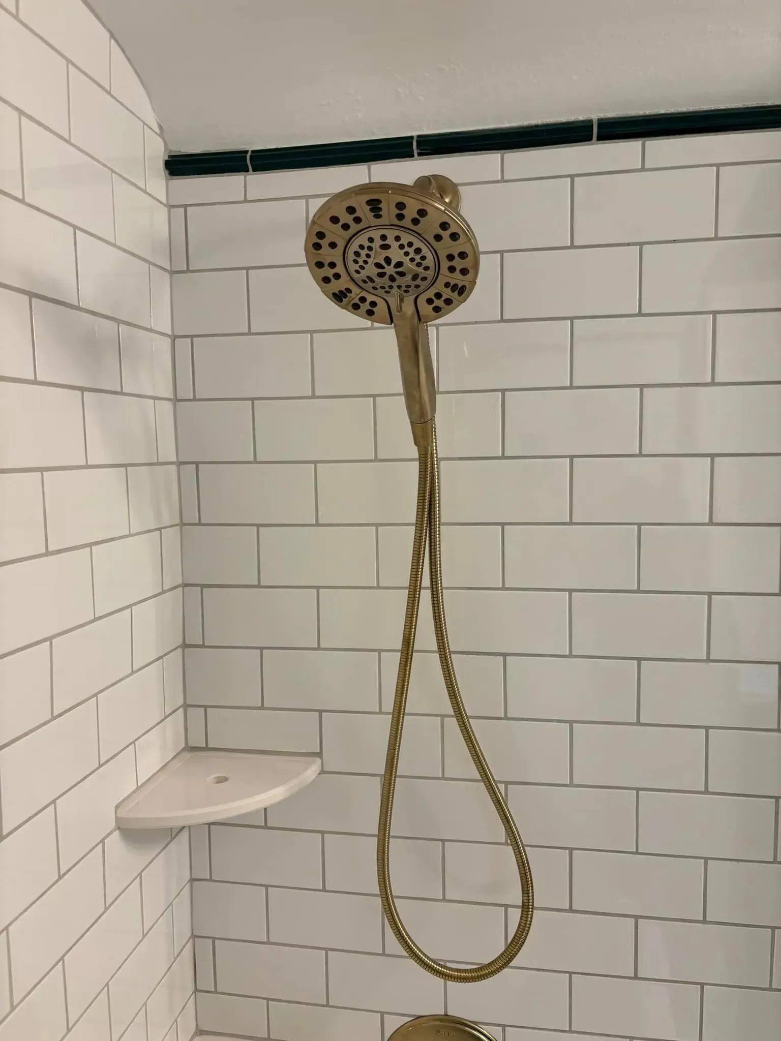 A shower head is hanging from the ceiling in a bathroom with white tiles.