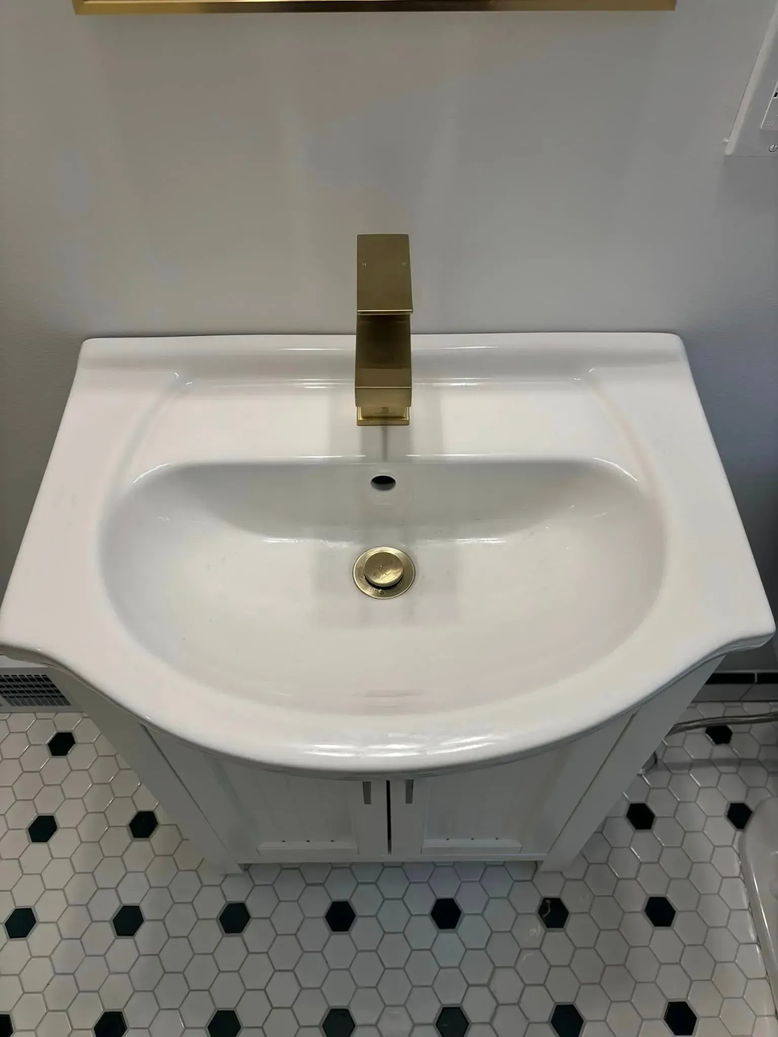 A bathroom sink with a gold faucet and a black and white tile floor.