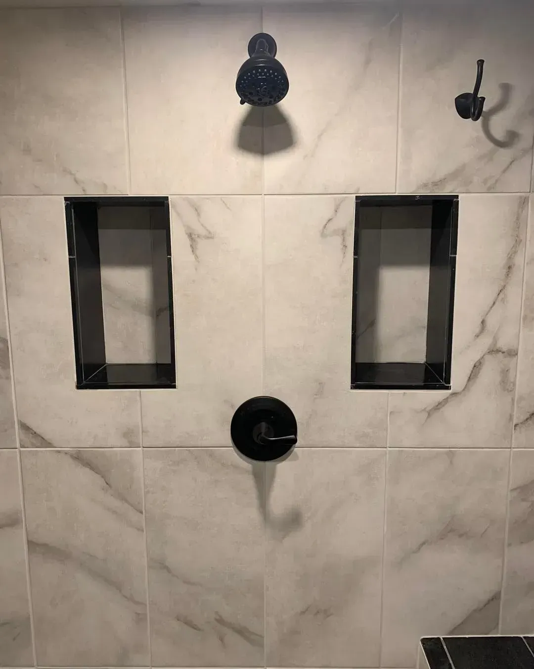A shower with two shelves and a black shower head