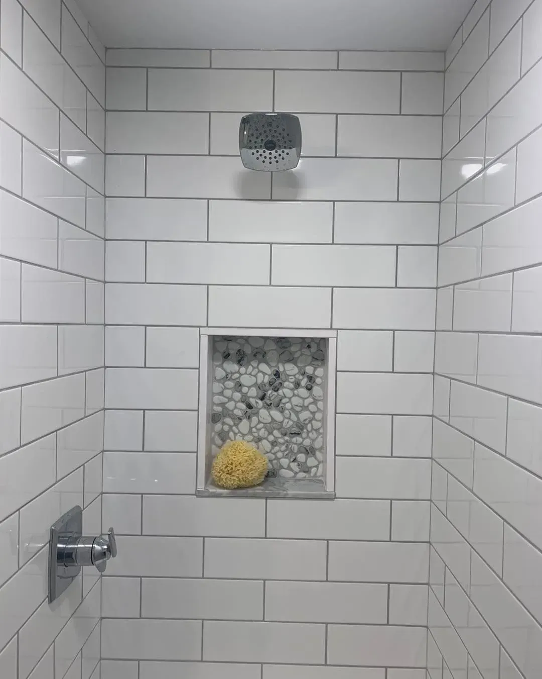 A shower with white tiles and a sponge in it.