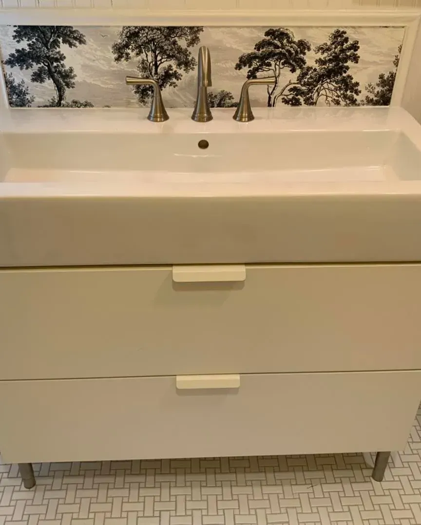 A bathroom sink with a picture of trees on the wall.