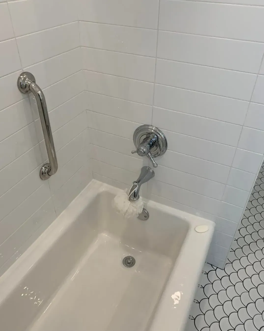 A bathtub with a handle on the side of it in a bathroom.