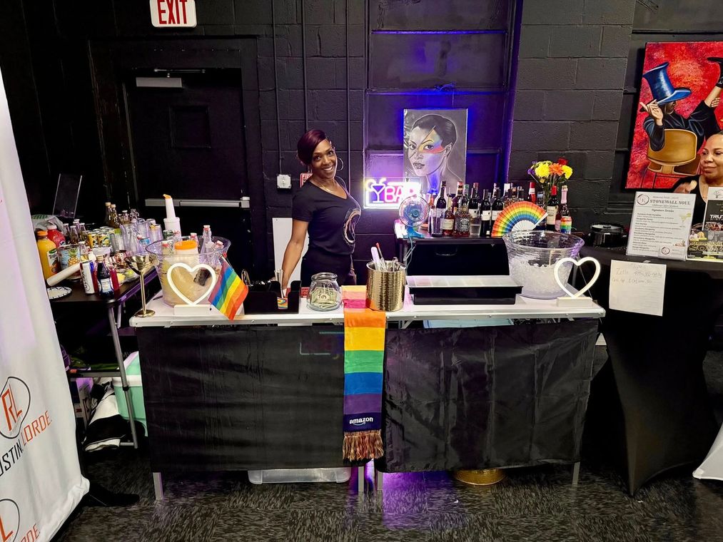 A woman is standing behind a bar with a rainbow flag on it.