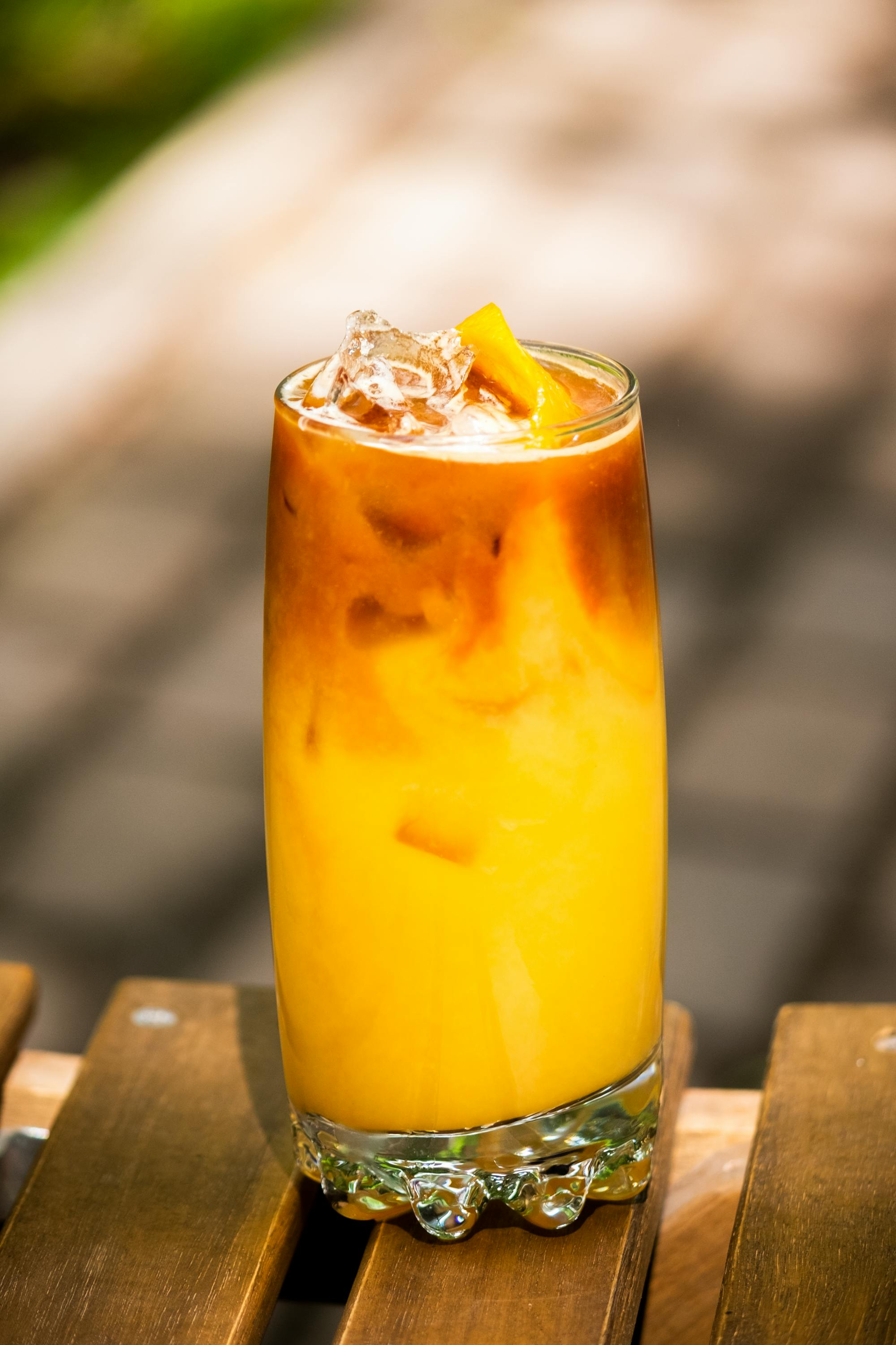 A glass of orange juice with ice is sitting on a wooden table.