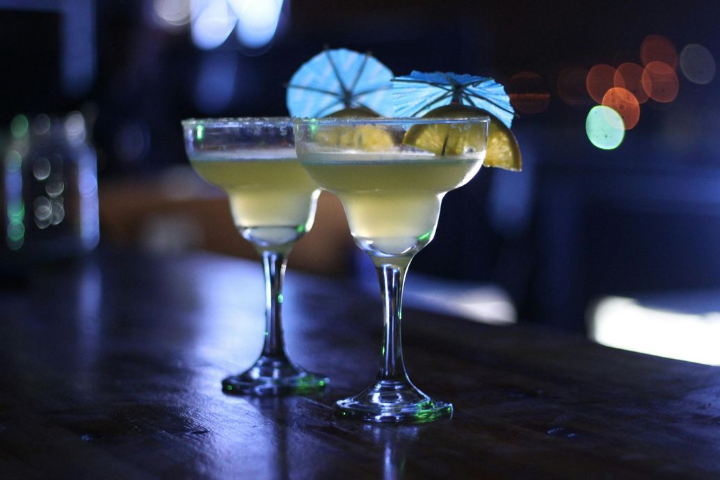 Two martini glasses with umbrellas on top of them on a bar.
