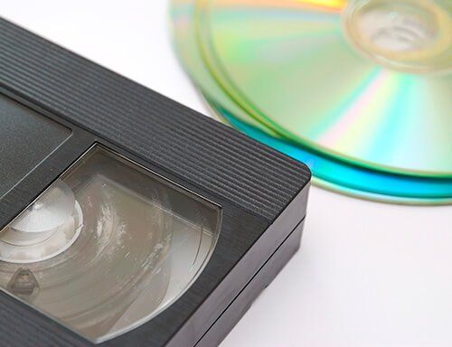 A vhs tape is sitting next to a cd on a white surface.