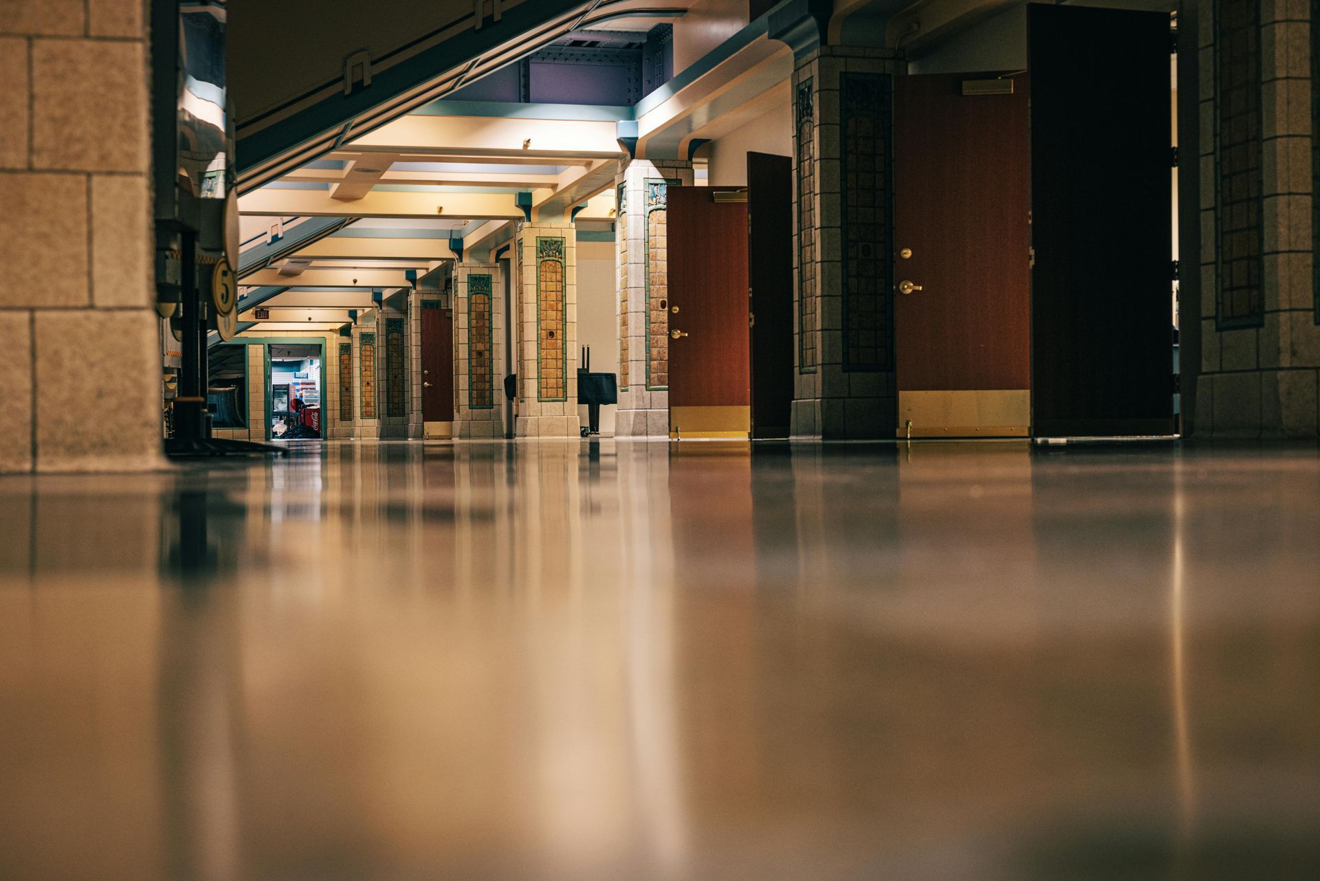 A low-angle view of a long, polished hallway in a building with stone columns, architectural lighting, and open doors.