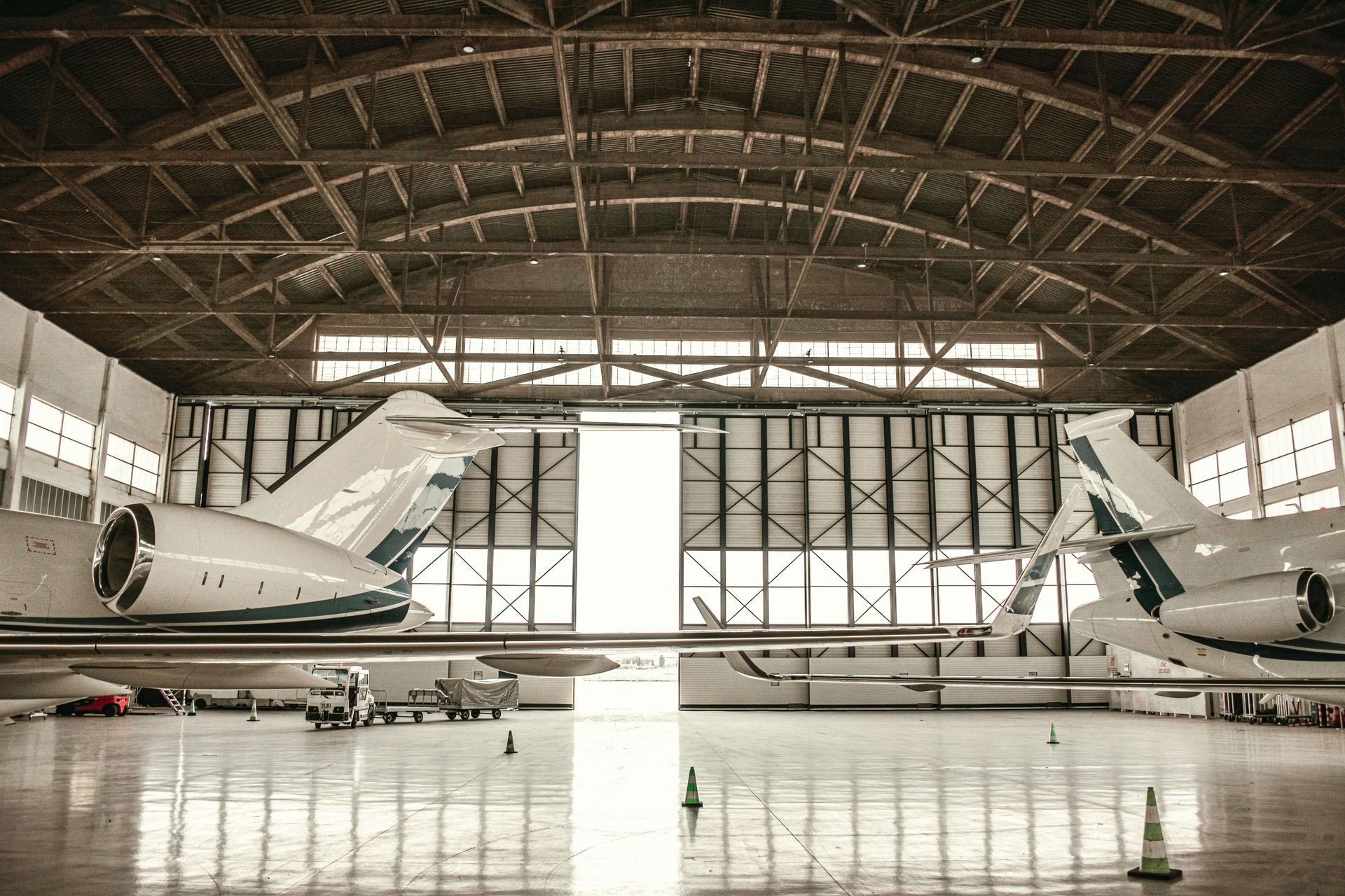 Two private jets parked inside a large, open-door aircraft hangar with a vaulted ceiling.  Epoxy floor