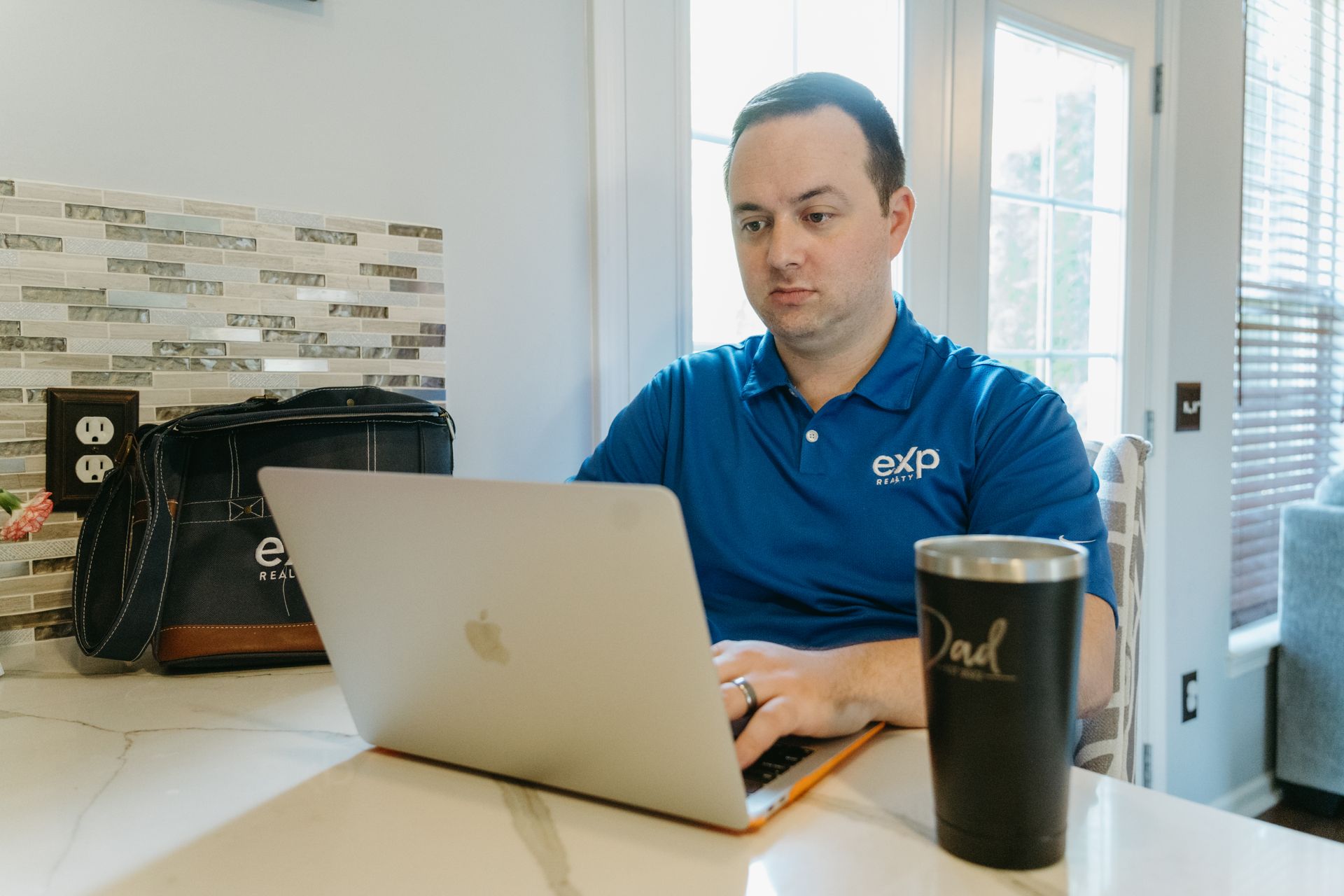 Man in blue shirt working on laptop at kitchen counter, with 