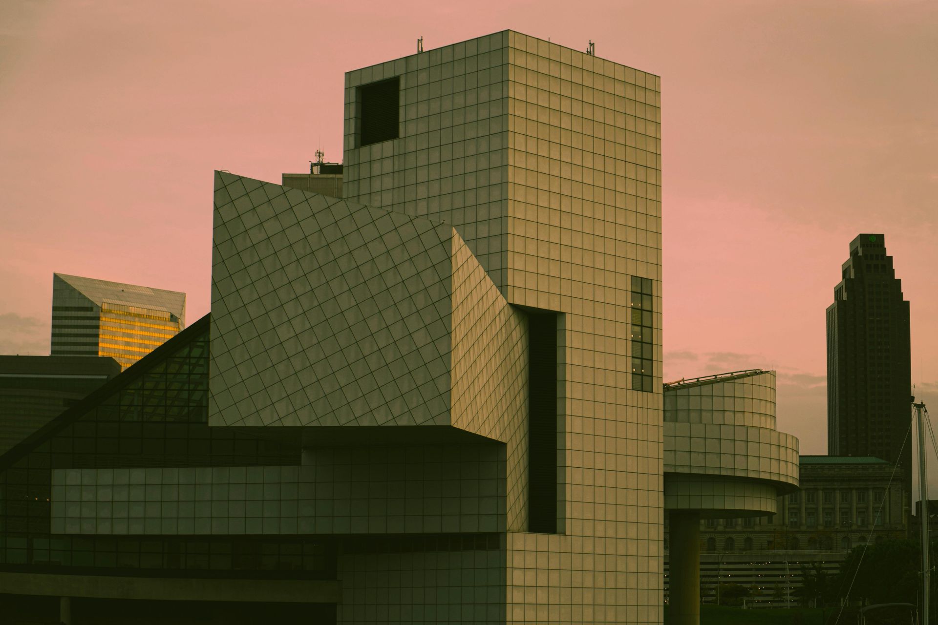 Rock and Roll Hall of Fame building in Cleveland, Ohio, with angular architecture, against a pink-hued sky.