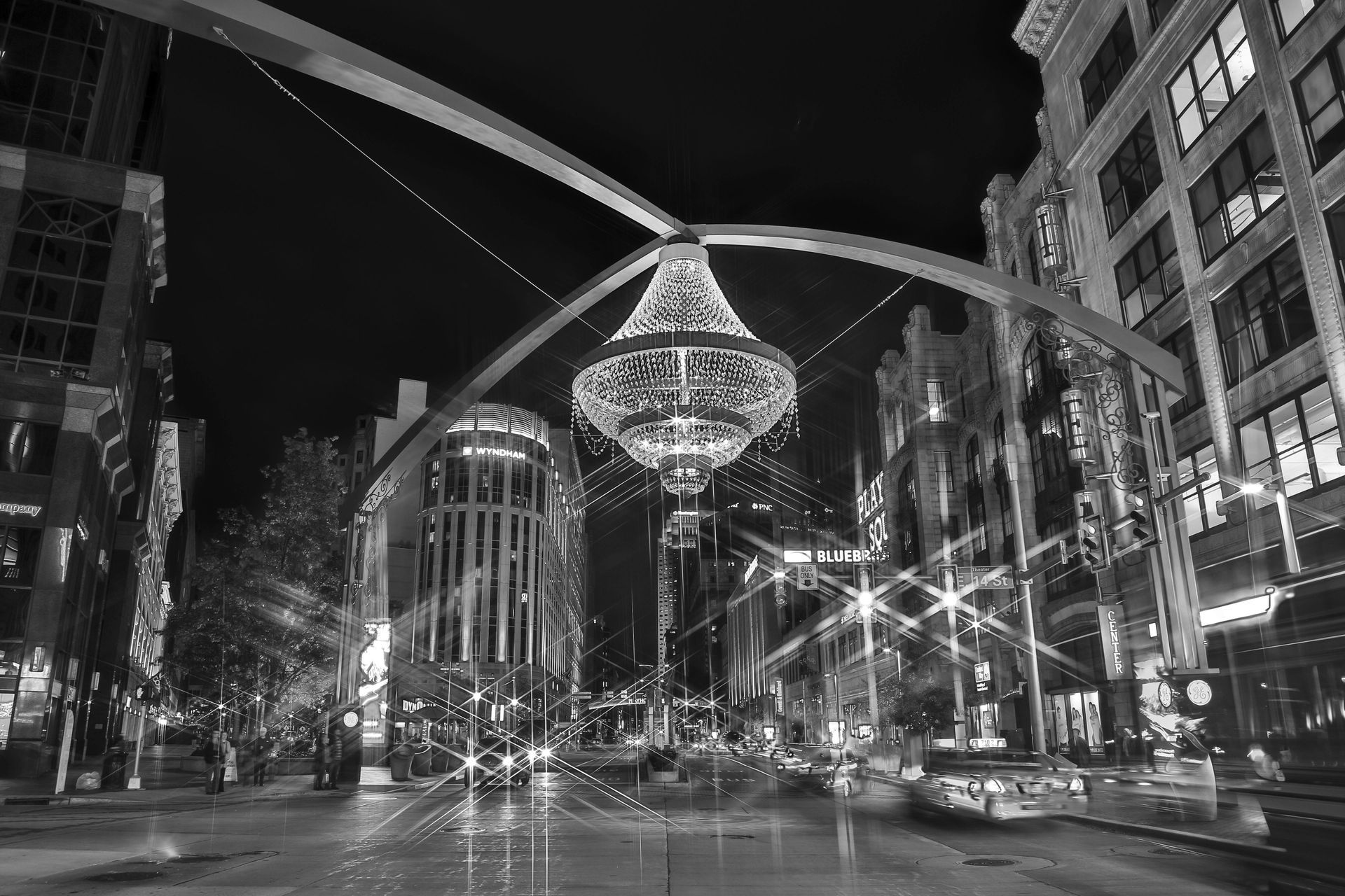 City street at night with large chandelier between tall buildings.