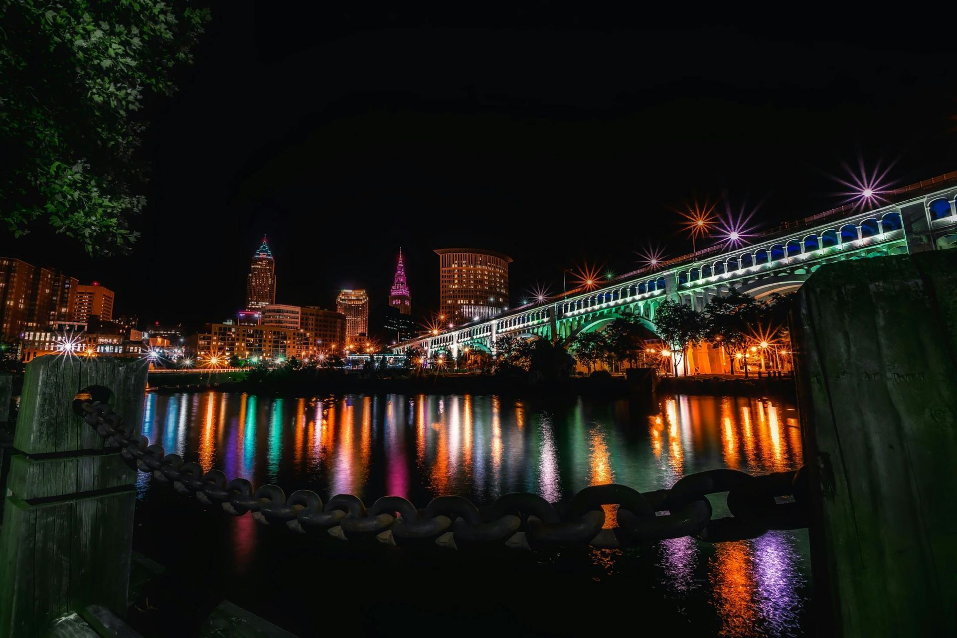 Night skyline of Cleveland with colorful lights reflected in the water. A bridge is illuminated.
