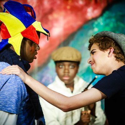 A man wearing a jester hat talks to another man