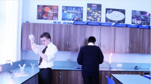 Two men are standing in a kitchen looking at a candle