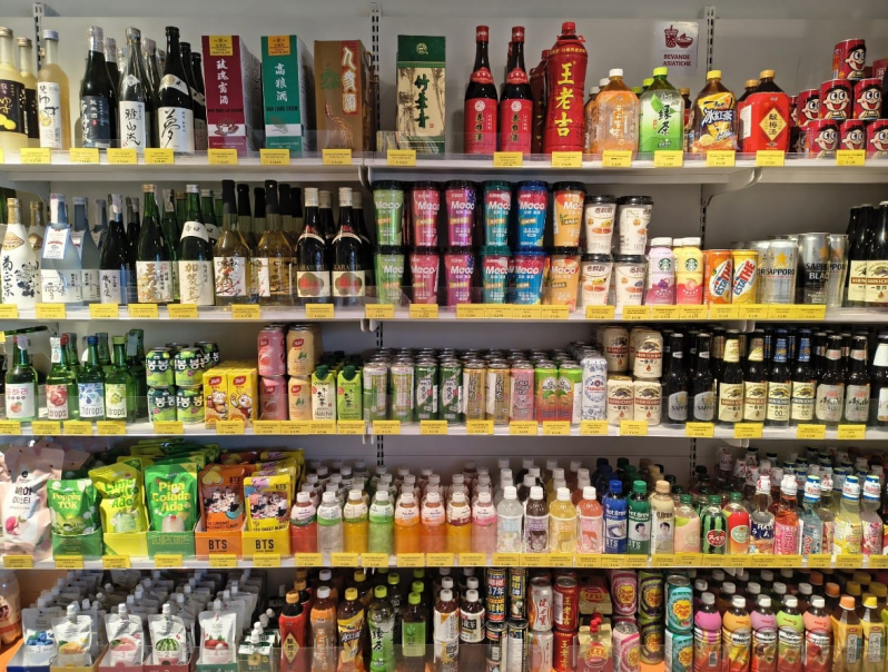 Uno scaffale di un supermercato pieno di bevande asiatiche e alcoliche in bottiglia e in lattina, dai colori vivaci.