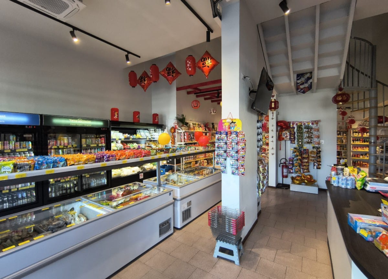 Interno di un negozio di alimentari asiatico con file di vetrine refrigerate, scaffali pieni di prodotti e decorazioni rosse appese.