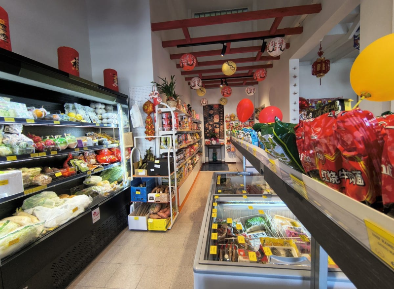 Vista interna di un negozio di alimentari con frigoriferi per frutta e verdura, scaffali pieni di prodotti, vetrine per surgelati e decorazioni festive.