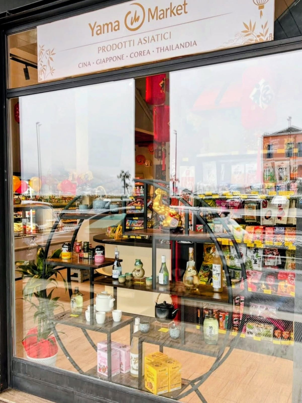La vetrina di Yama Market, un negozio di alimentari asiatico, con scaffali pieni di servizi da tè e altri articoli.
