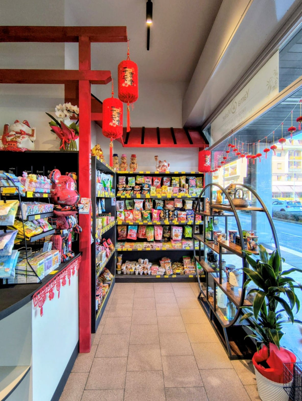 Vista interna di un negozio decorato con motivi di ispirazione asiatica, caratterizzato da archi torii rossi, lanterne e scaffali per snack.