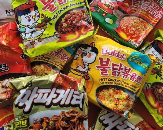 Un primo piano di una pila di diverse confezioni di ramen istantaneo coreano, caratterizzate da colori vivaci e dal logo con mascotte a cartoni animati.