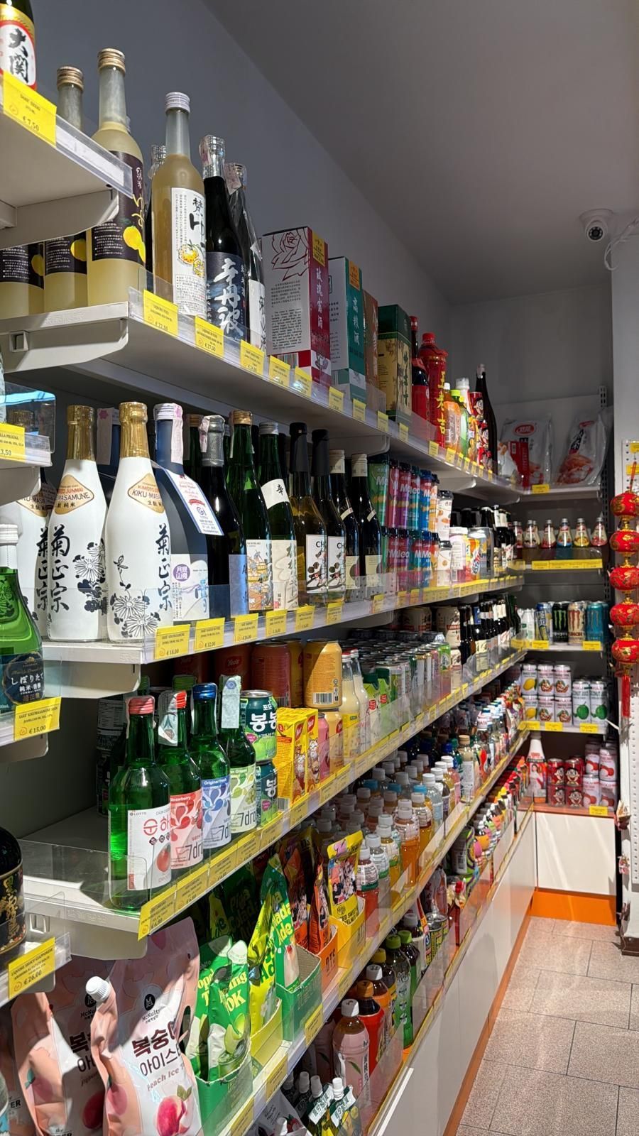 In un mercato, gli scaffali sono pieni di varie bottiglie di vetro di liquori e sakè, con contenitori più piccoli visibili sulla destra.