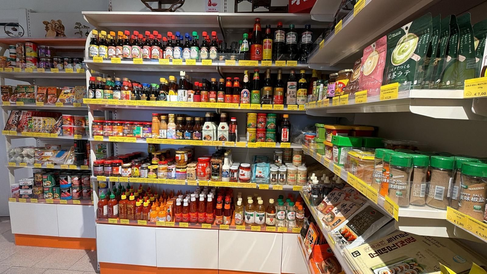 Scaffali pieni di salse in bottiglia di vario tipo, condimenti e prodotti alimentari confezionati in un corridoio di un supermercato.