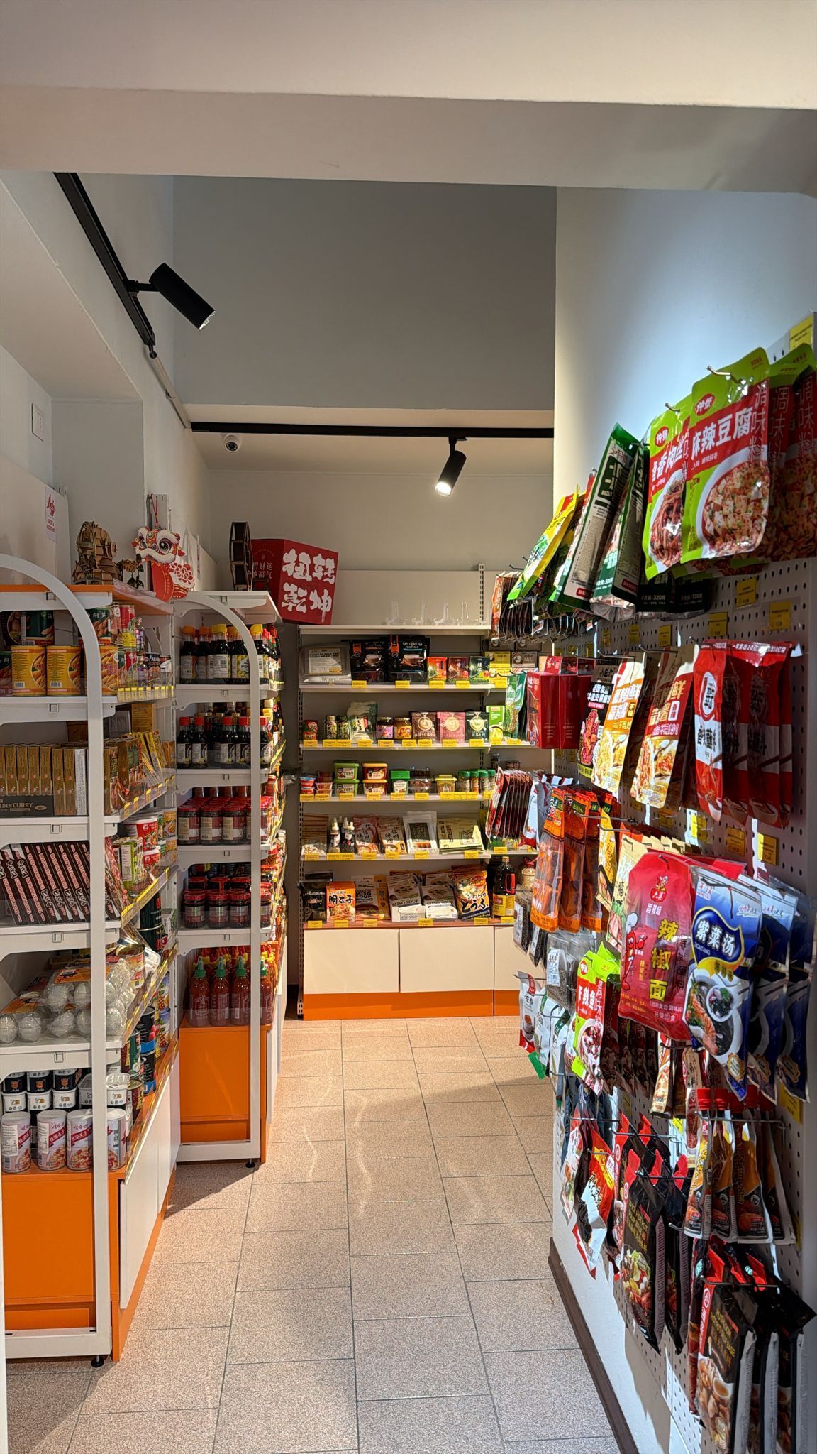 Uno stretto corridoio in un negozio di alimentari asiatico, con scaffali pieni di snack e prodotti confezionati su entrambi i lati.