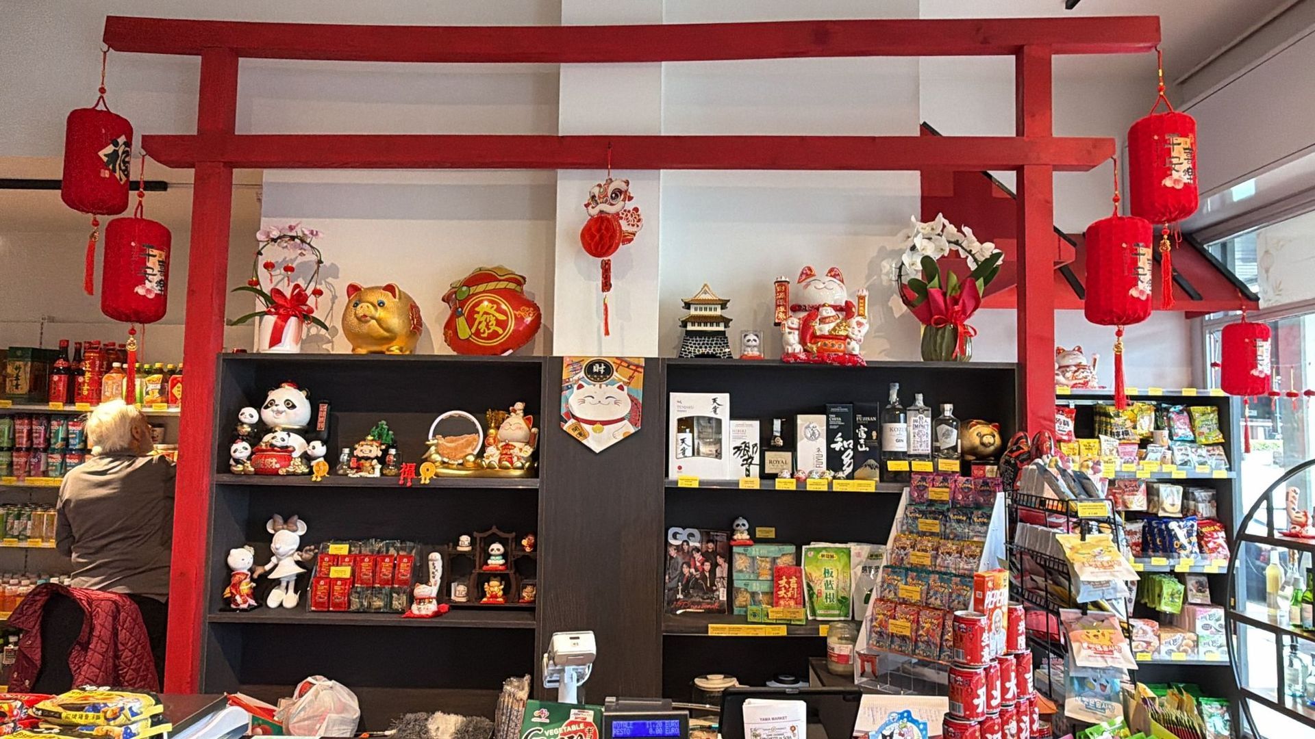 Interno del negozio caratterizzato da scaffali pieni di prodotti asiatici, incorniciati da un imponente portale torii rosso in stile giapponese.