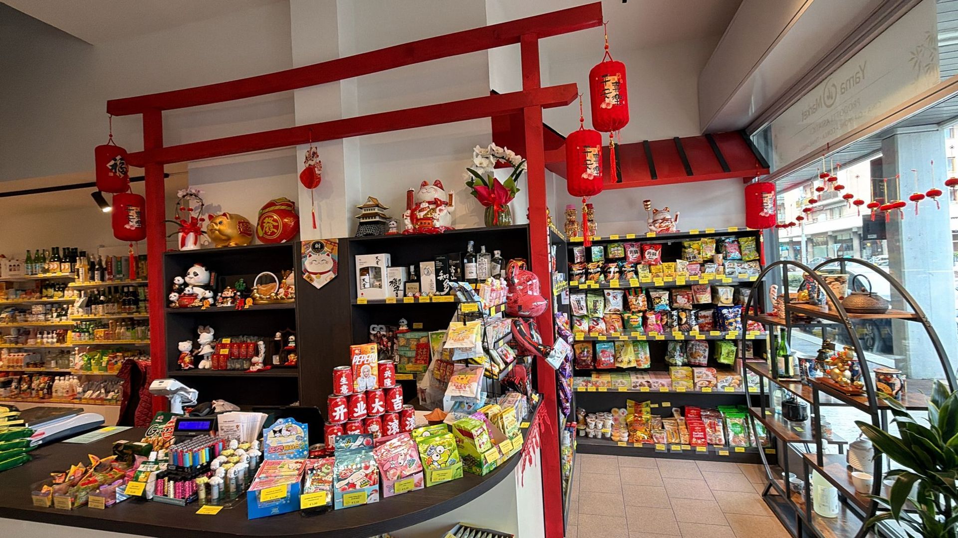 L'interno di un negozio in stile asiatico caratterizzato da un'architettura con portali torii rossi, lanterne appese e scaffali pieni di snack.