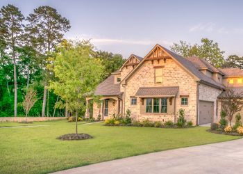 A large house with a lush green lawn and trees in the background.