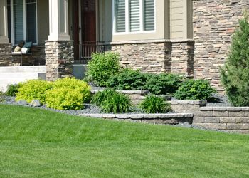 A house with a lush green lawn and a stone wall in front of it.