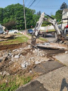 An excavator is digging a hole in the ground on the side of the road.