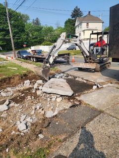 A man is driving a small excavator on a sidewalk.