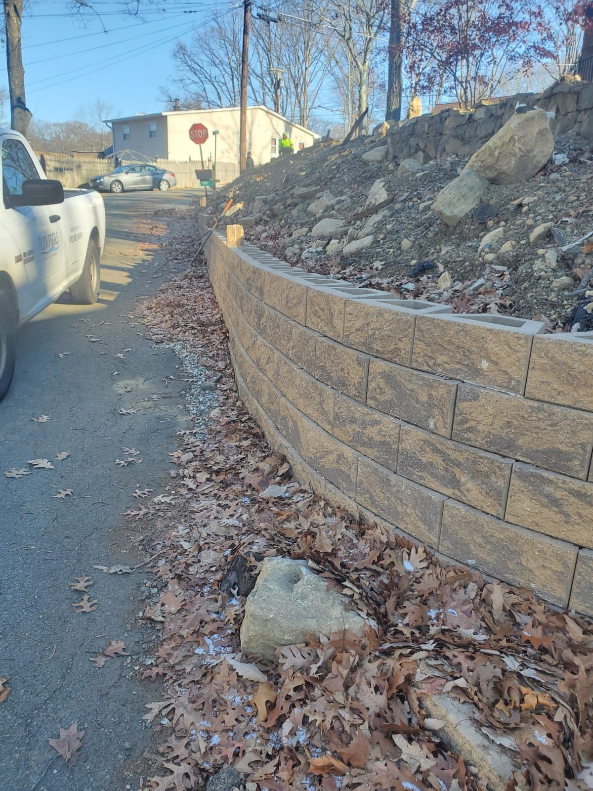A white truck is parked on the side of the road next to a retaining wall.