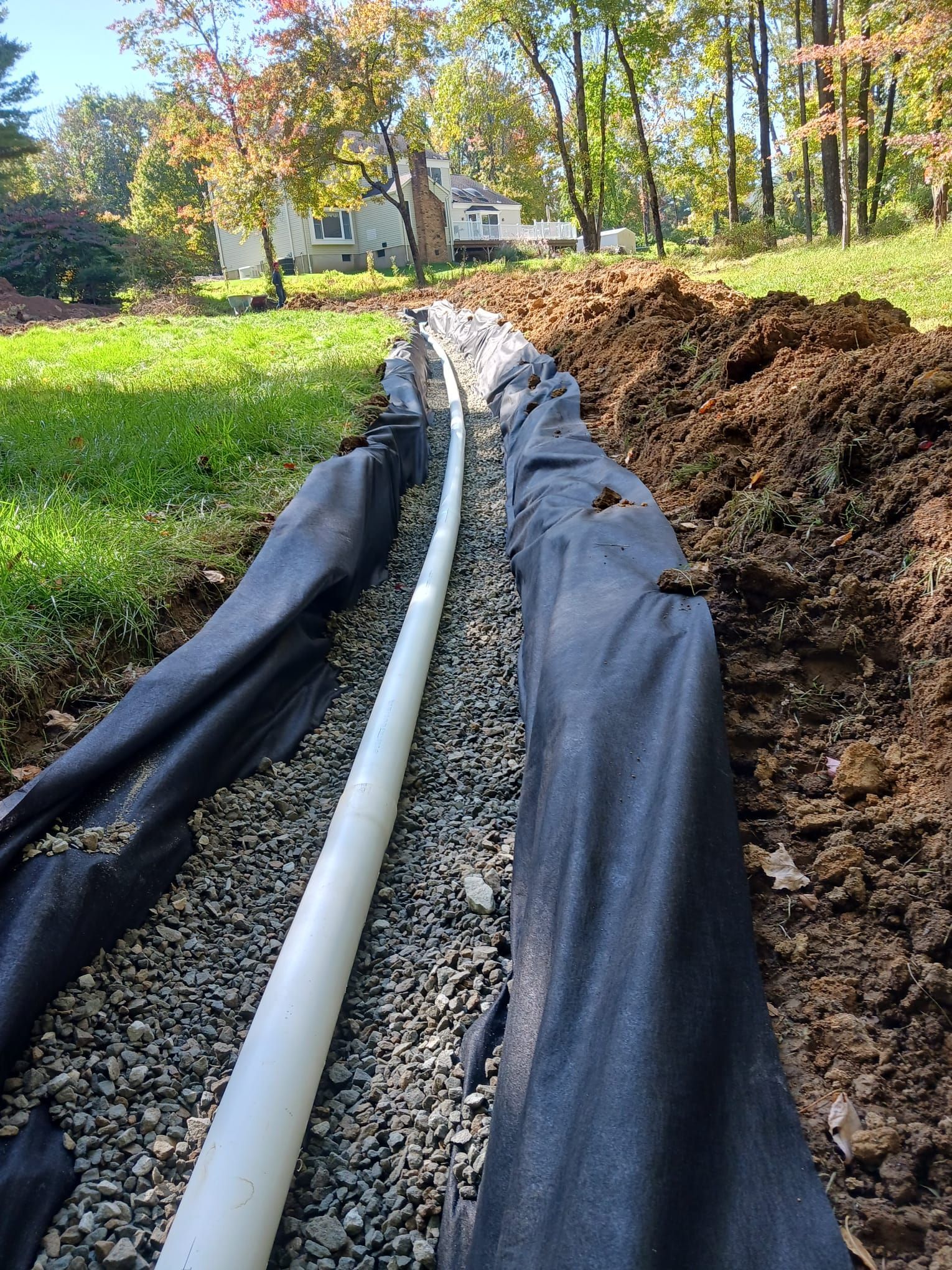 A white pipe is laying in the dirt next to a black tarp.