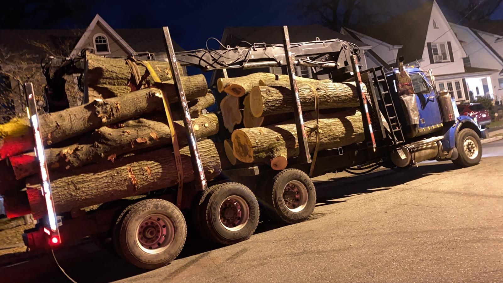 A large log truck is parked on the side of the road at night.