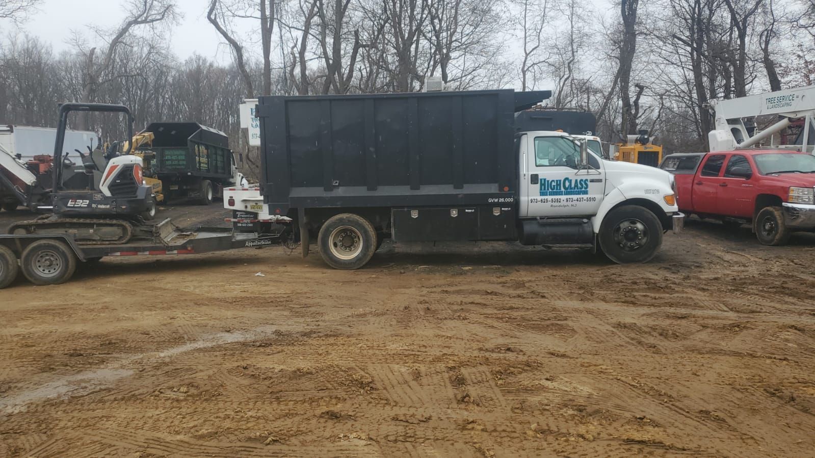 A dump truck is being towed by a trailer in a dirt field.