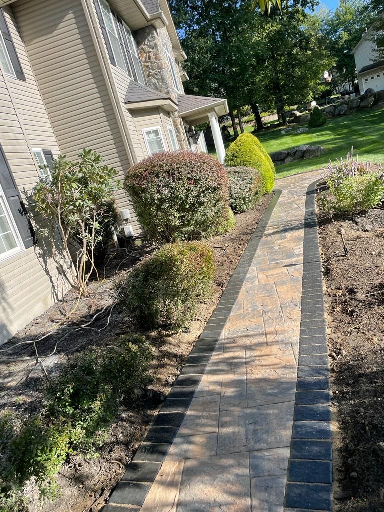 A brick walkway leading to a house surrounded by bushes and trees.