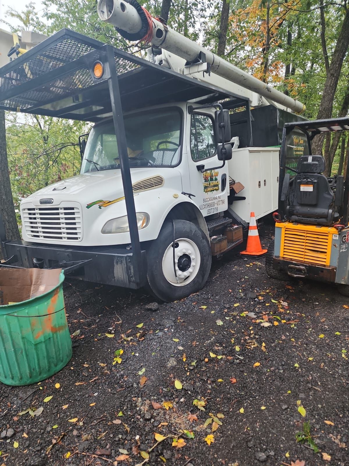 A white truck is parked next to a forklift in a parking lot.