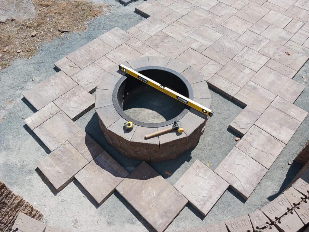 A fire pit is being built on a patio with bricks and a level.