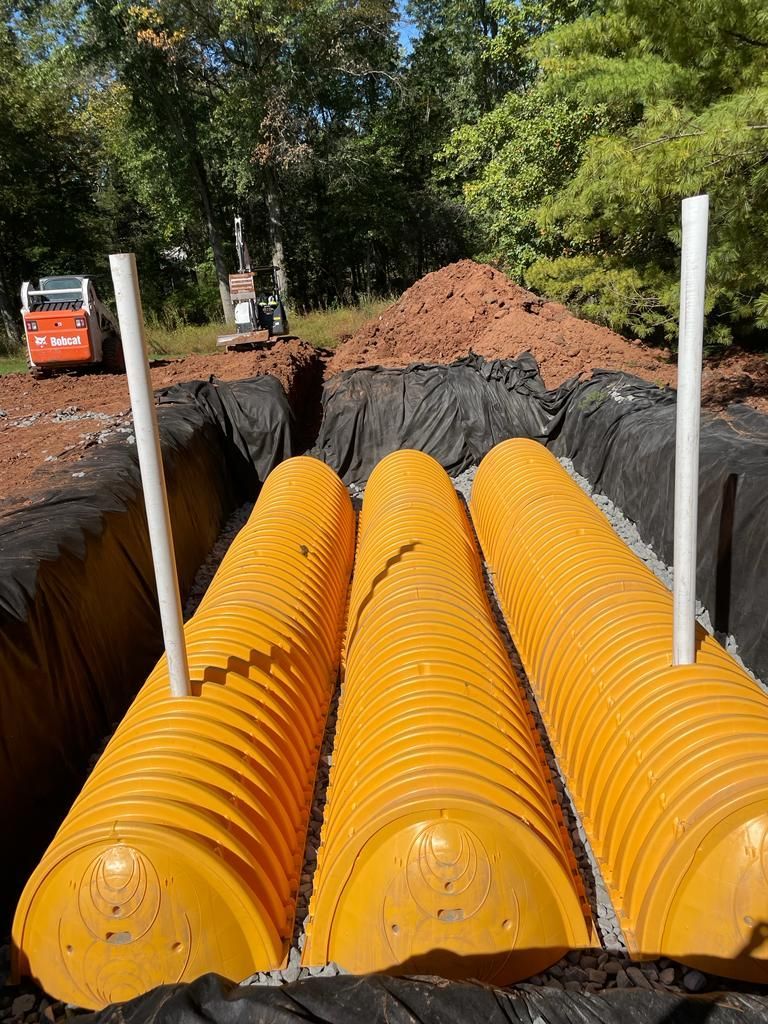 A bunch of yellow pipes are sitting in a trench.