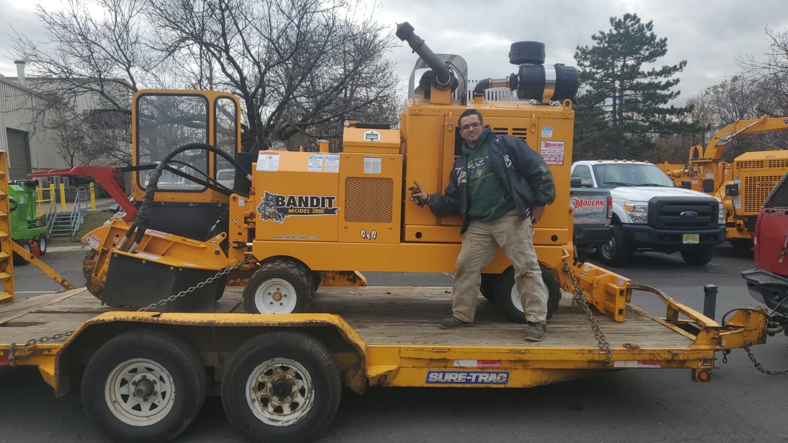 A man is standing next to a yellow machine on a trailer.