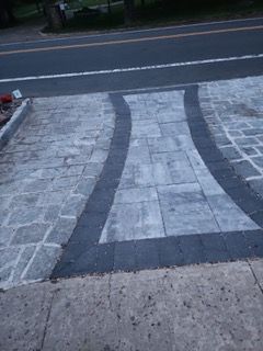 A brick driveway with a black border is next to a road.